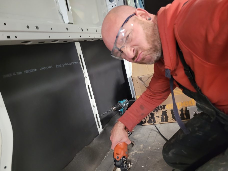 Ein Mann in Schutzbrille schneidet mit einem Werkzeug in einem Innenraum.