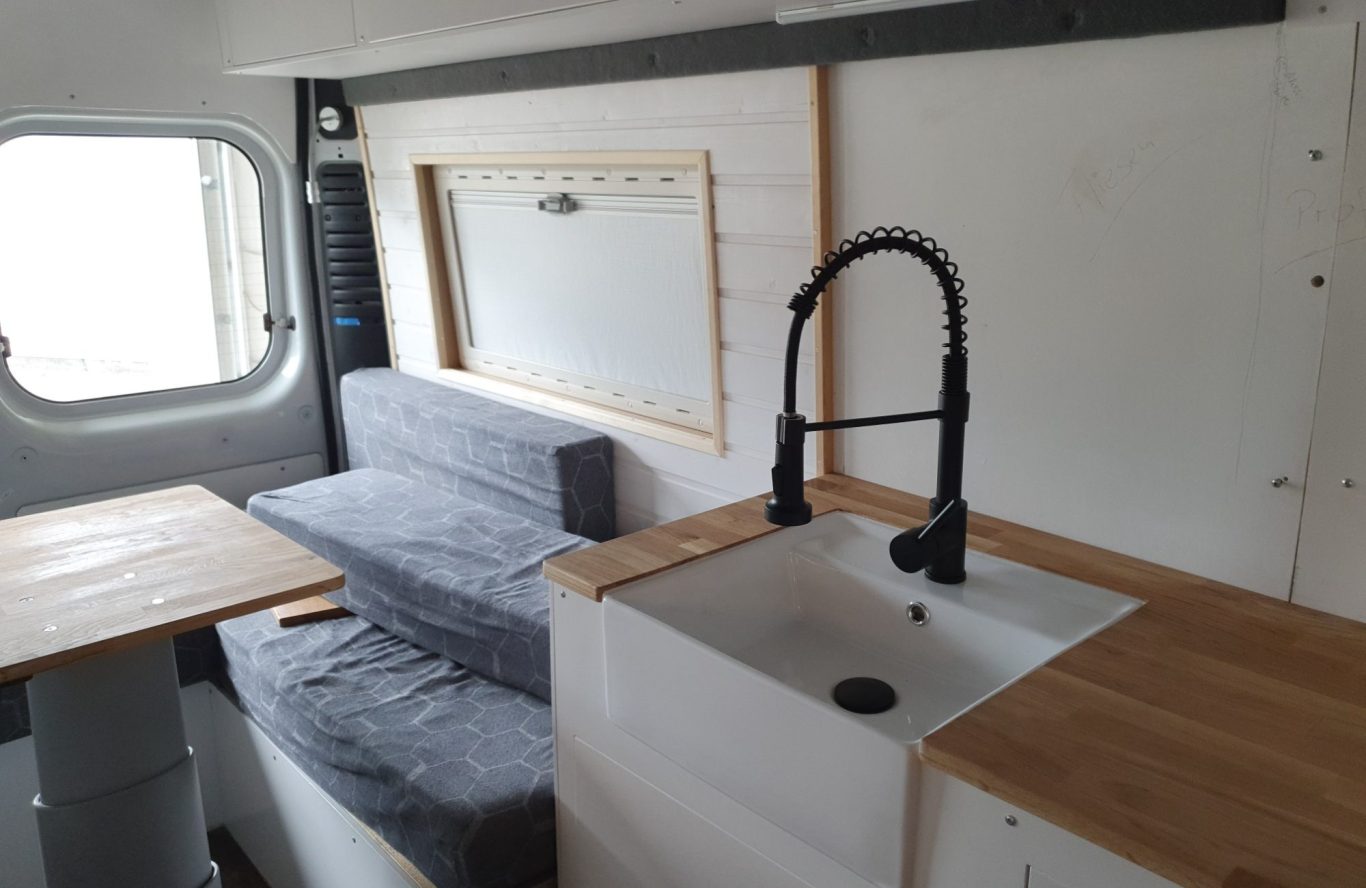 Camper mit Holzausbau Moderne Campingküche mit Spüle, Sitzbereich und Holzoberflächen.
