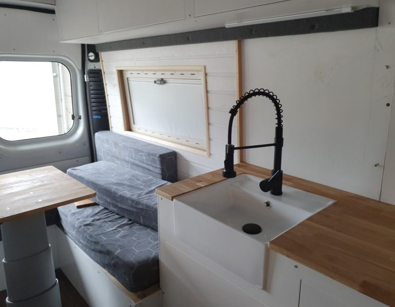 Minimalist Innenraum eines Wohnmobils mit Küchenzeile, Essbereich und Sitzecke.