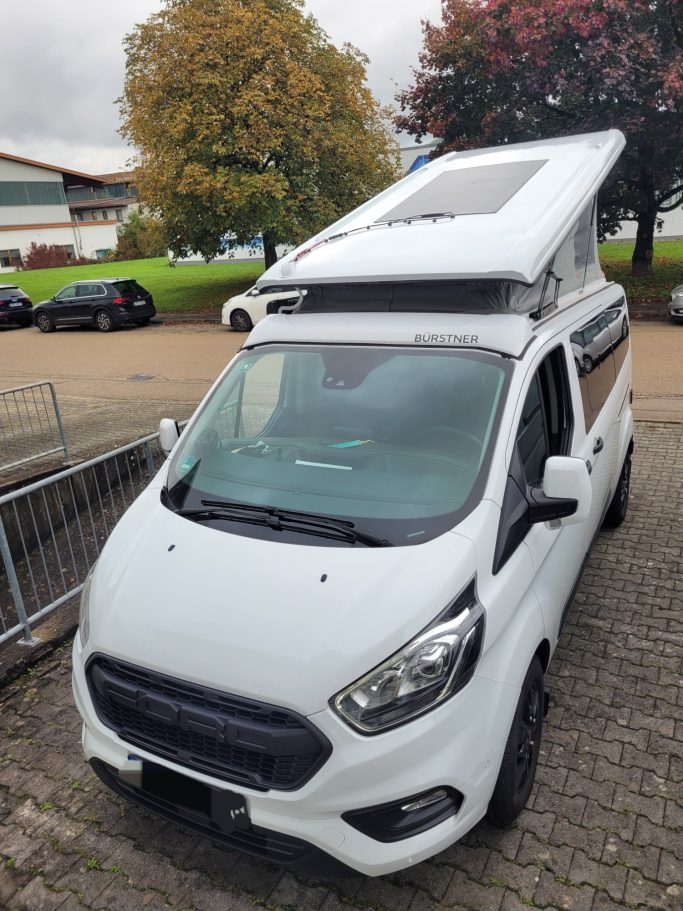Weißer Campingbus mit faltbarem Dach und Solarpanel.