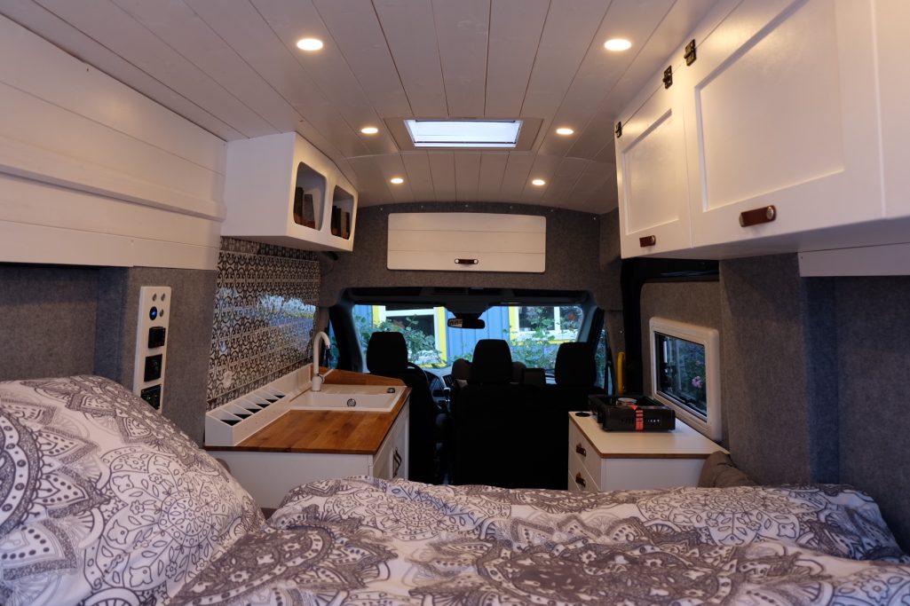 Kompakte Wohnmobil-Innenansicht mit Küche und Bett, modern und gemütlich eingerichtet.