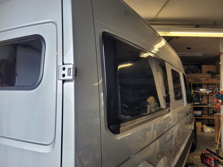 Grauer Lieferwagen mit offenen Fenstern in einer Werkstatt.